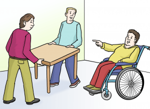 Ein Mann im Rollstuhl zeigt auf zwei Menschen, die einen Tisch tragen.