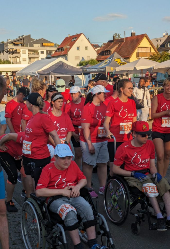 Eine Gruppe von Menschen mit Roten T-Shirts und Atrio Logo, dabei auch zwei Rollstuhlfahrer. Alle haben Startnummern.
