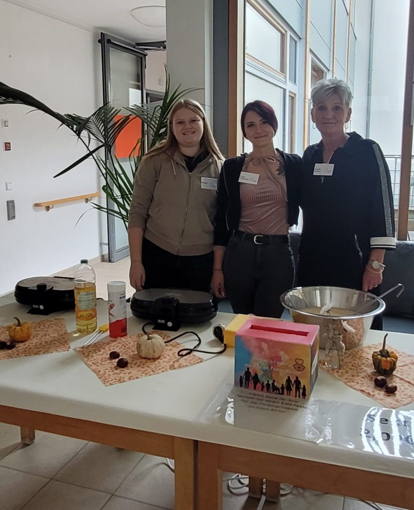 3 Frauen stehen an einem Tisch mit Waffeleisen und einer großen Teigschüssel.