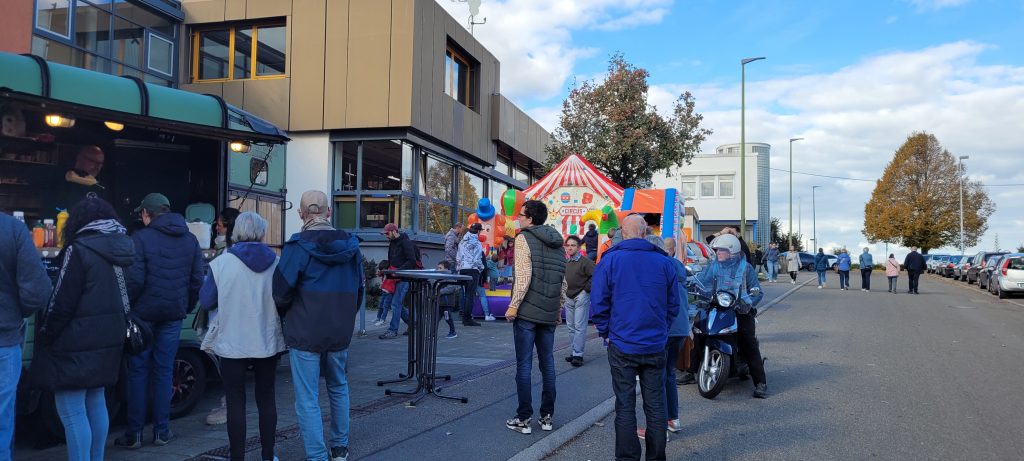 Viele Menschen sind auf der Straße vor der Werkstatt. Im Vordergrund steht ein Food Truck, im Hintergrund eine Hüpfburg.