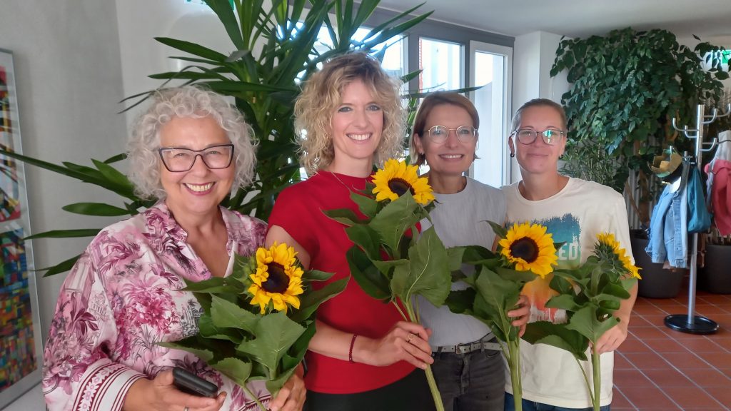4 Frauen lächeln in die Kamera und halten jeweils eine große Sonnenblume in der Hand.