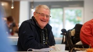 Senior sitzt lächelnd bei einer Tasse Kaffee in heller Seniorentagesbetreuung